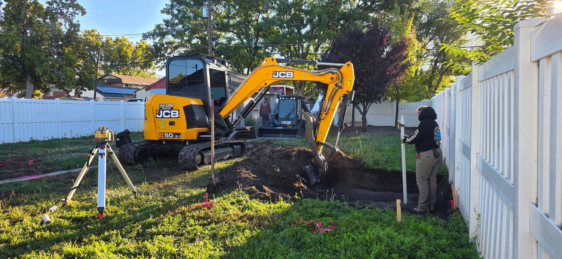 J&J grading a residential site with a JCB excavator while checking layout and elevation